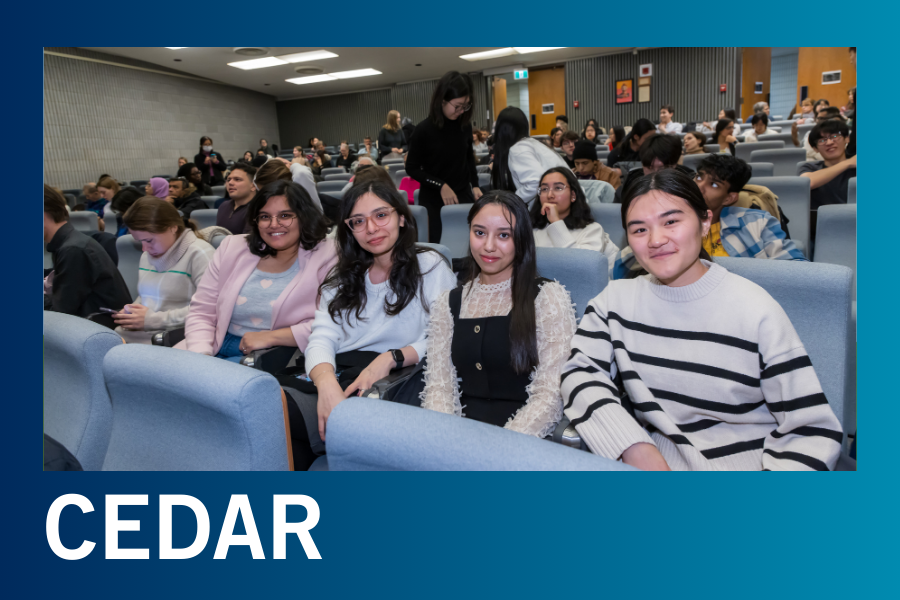 Students sitting in a lecture hall smiling at the camera